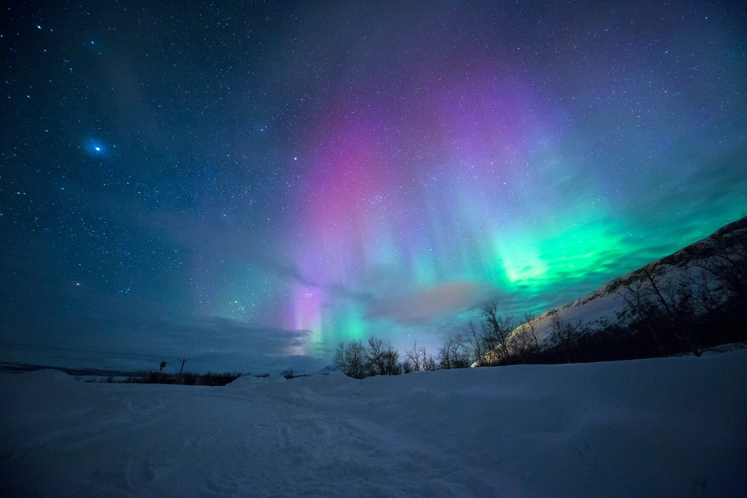 Zelená a fialová polárna tiara na nočnej oblohe nad zasneženou keajinou na Islande.